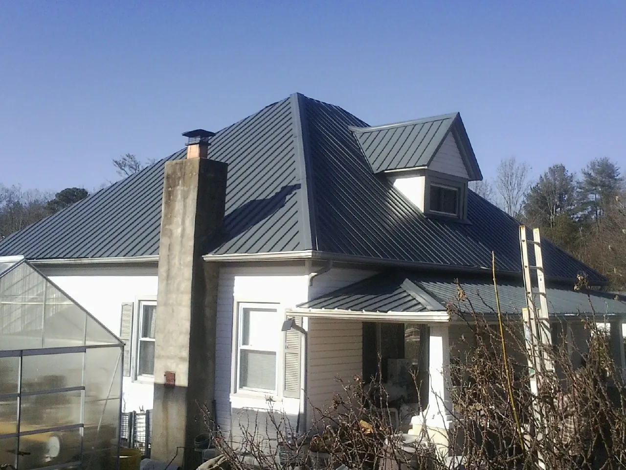 Dark blue standing seam metal roof on a white farmhouse with dormer — Slate & Tile Roof Repair by Roofing Brothers in Jarratt