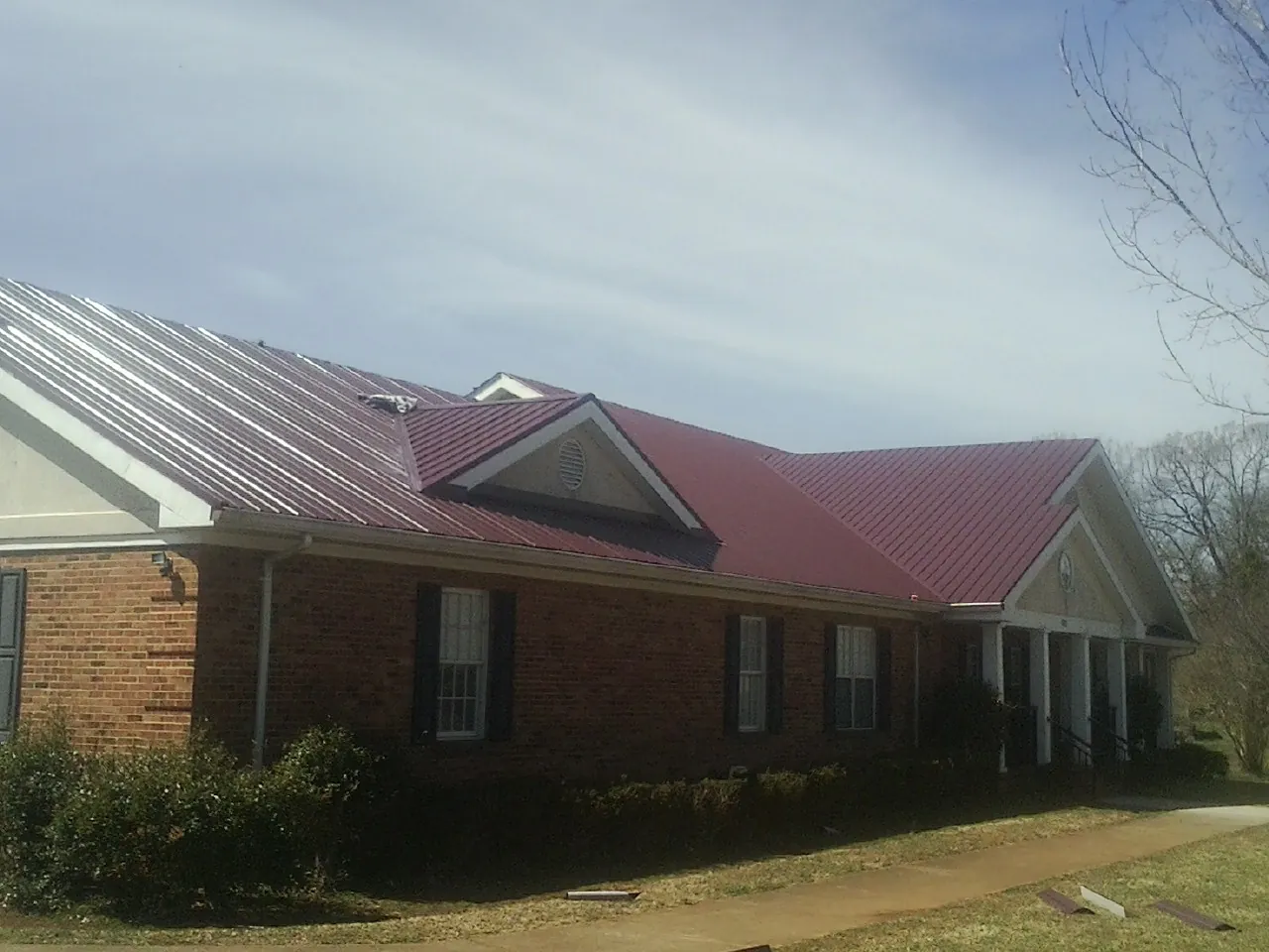 Red metal roof with gabled entries on a long brick building, from a Hail Damage Roof Repair job in Jarratt