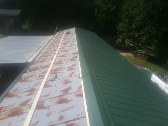 Old rusted panels beside newly installed green metal roofing — Wind Damage Roof Repair by Roofing Brothers in Jarratt