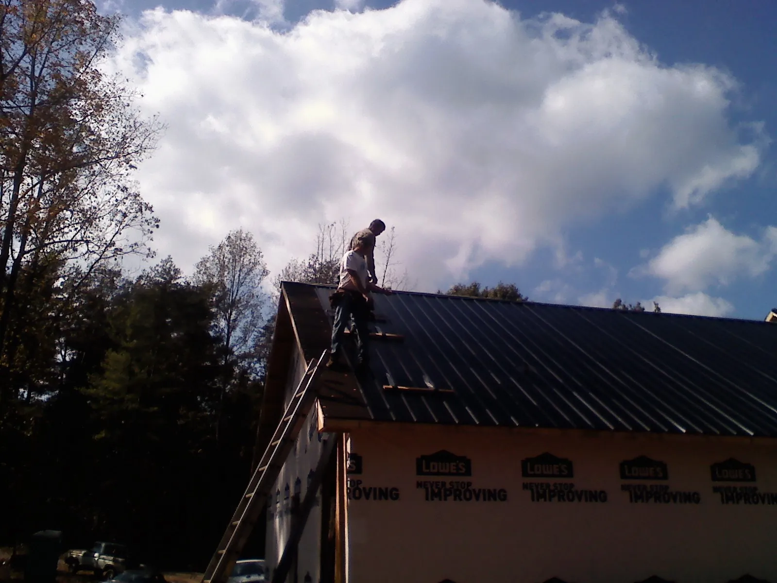 Roofer fastening dark metal panels high against a cloudy sky, from a Roof Inspection job in Jarratt