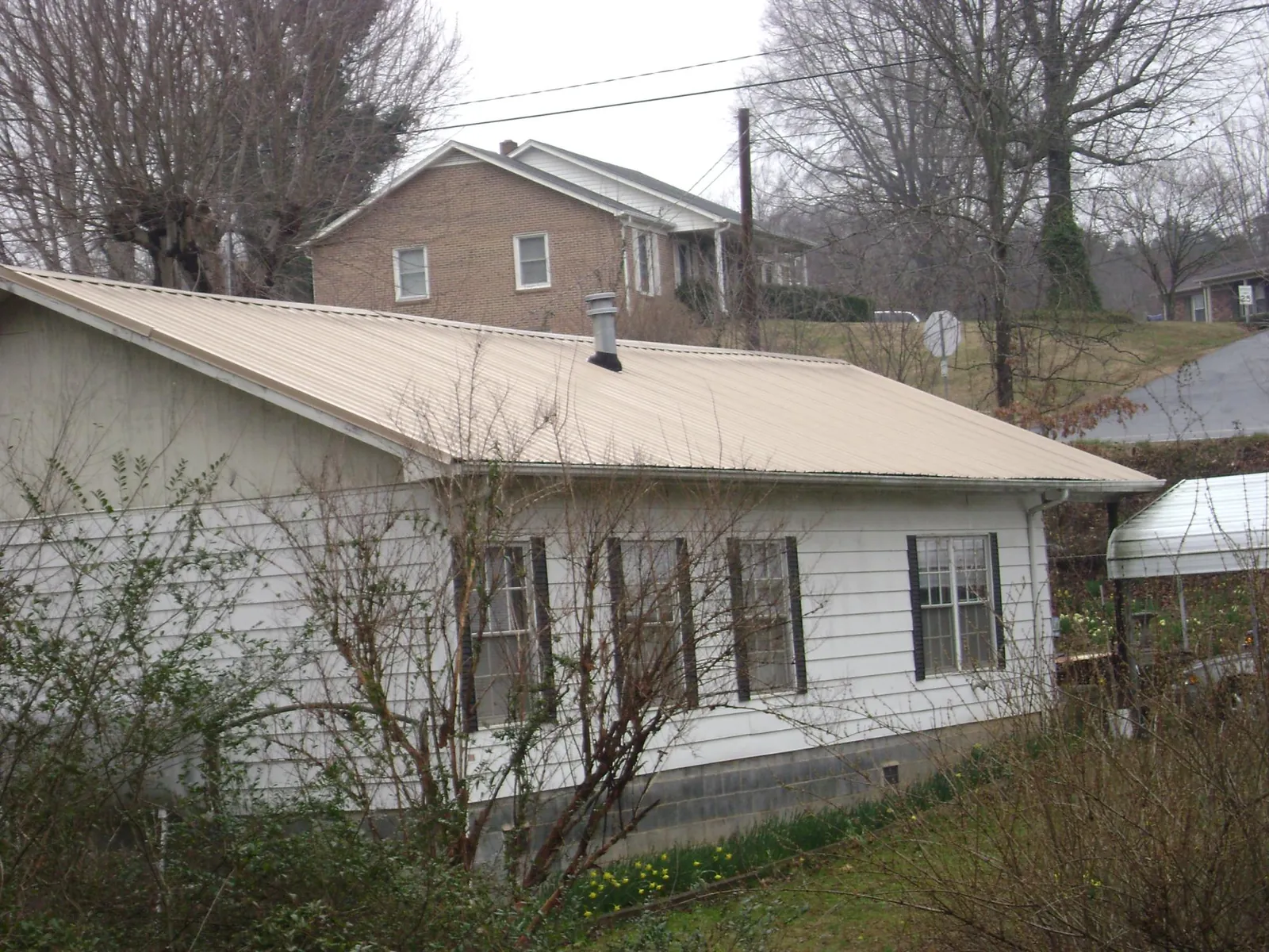 Tan metal roof on a white sided house set into a hillside — Commercial Roofing by Roofing Brothers in Jarratt